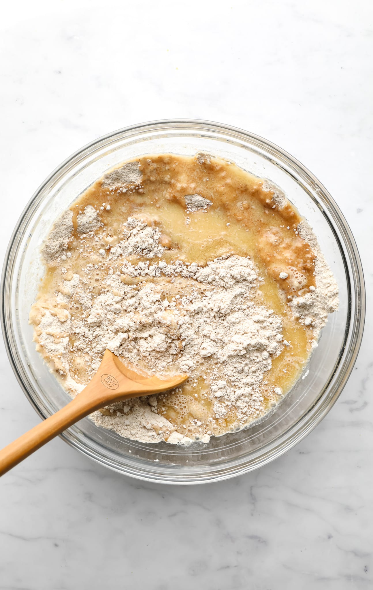 using a wooden spoon to stir vegan apple muffin batter in a glass bowl.