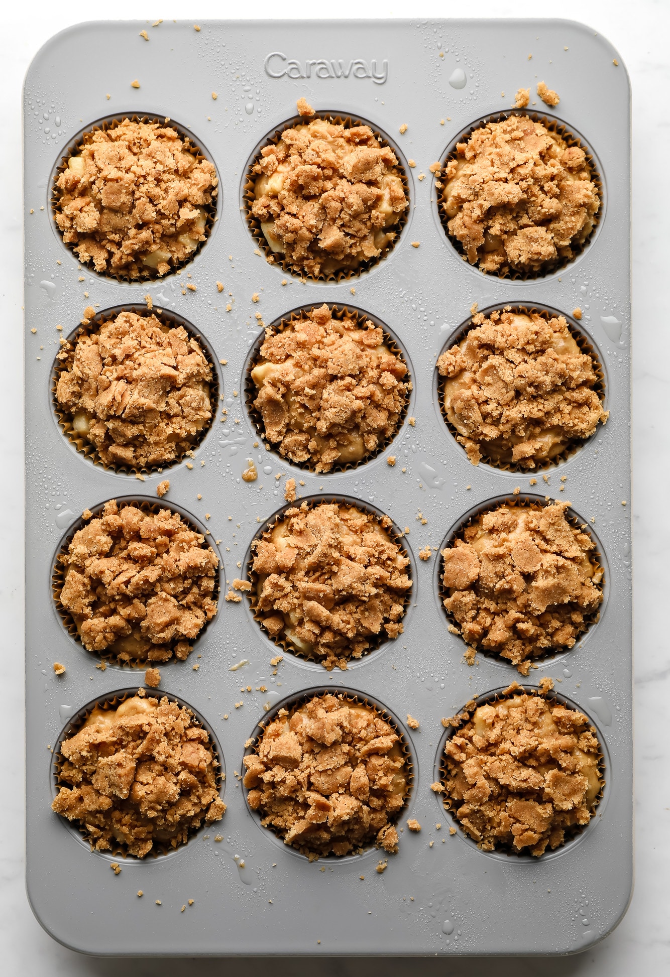 vegan apple muffins topped with a crumble topping in a muffin tin.