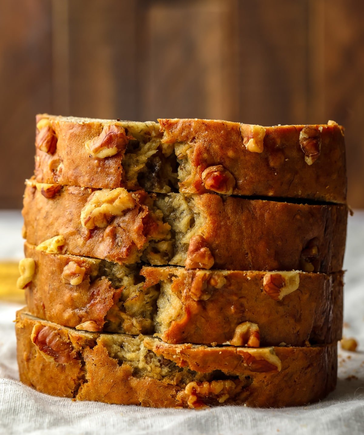 stacked sliced vegan banana bread with walnuts throughout, wood backdrop