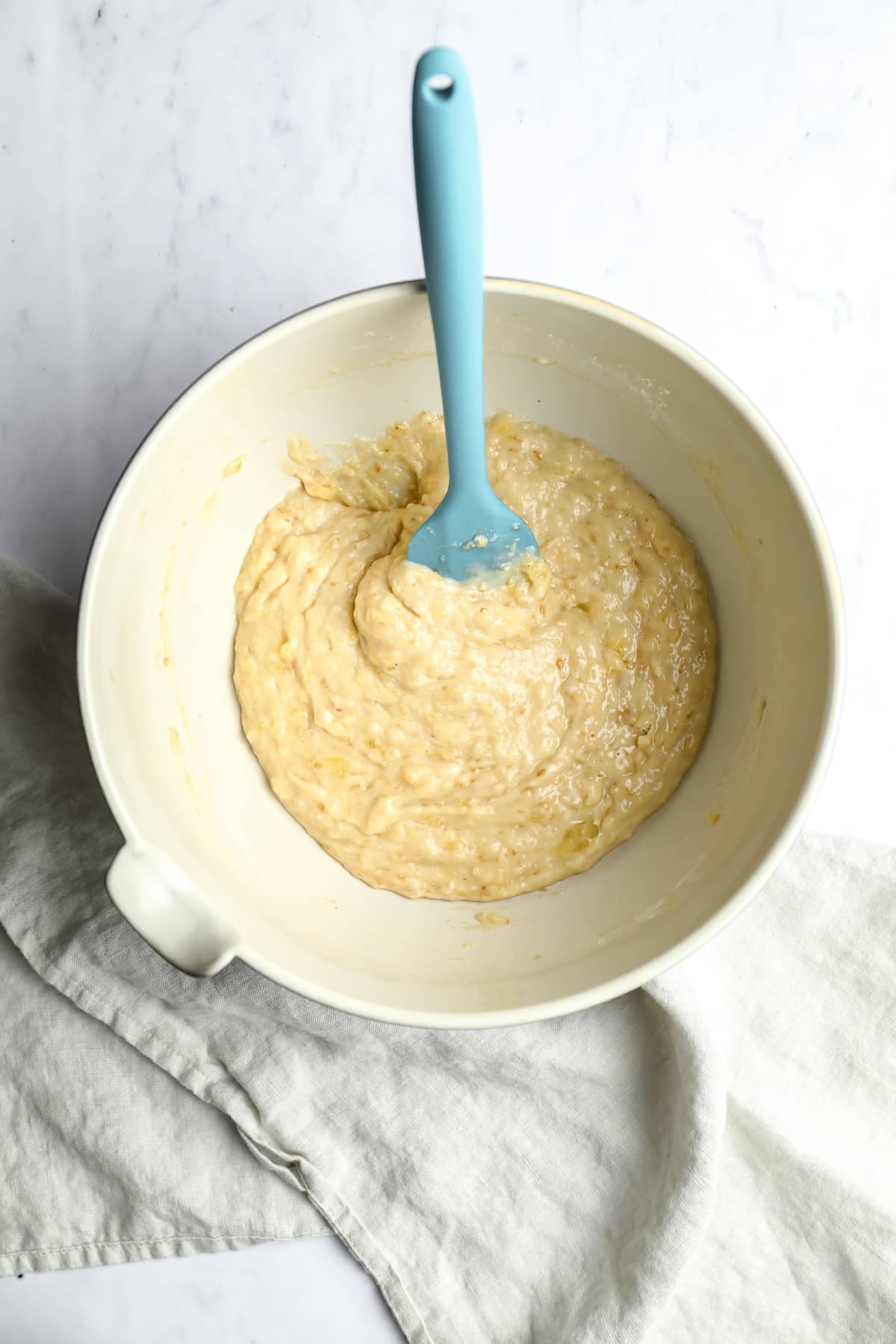 bowl of banana bread batter with blue spatula in it