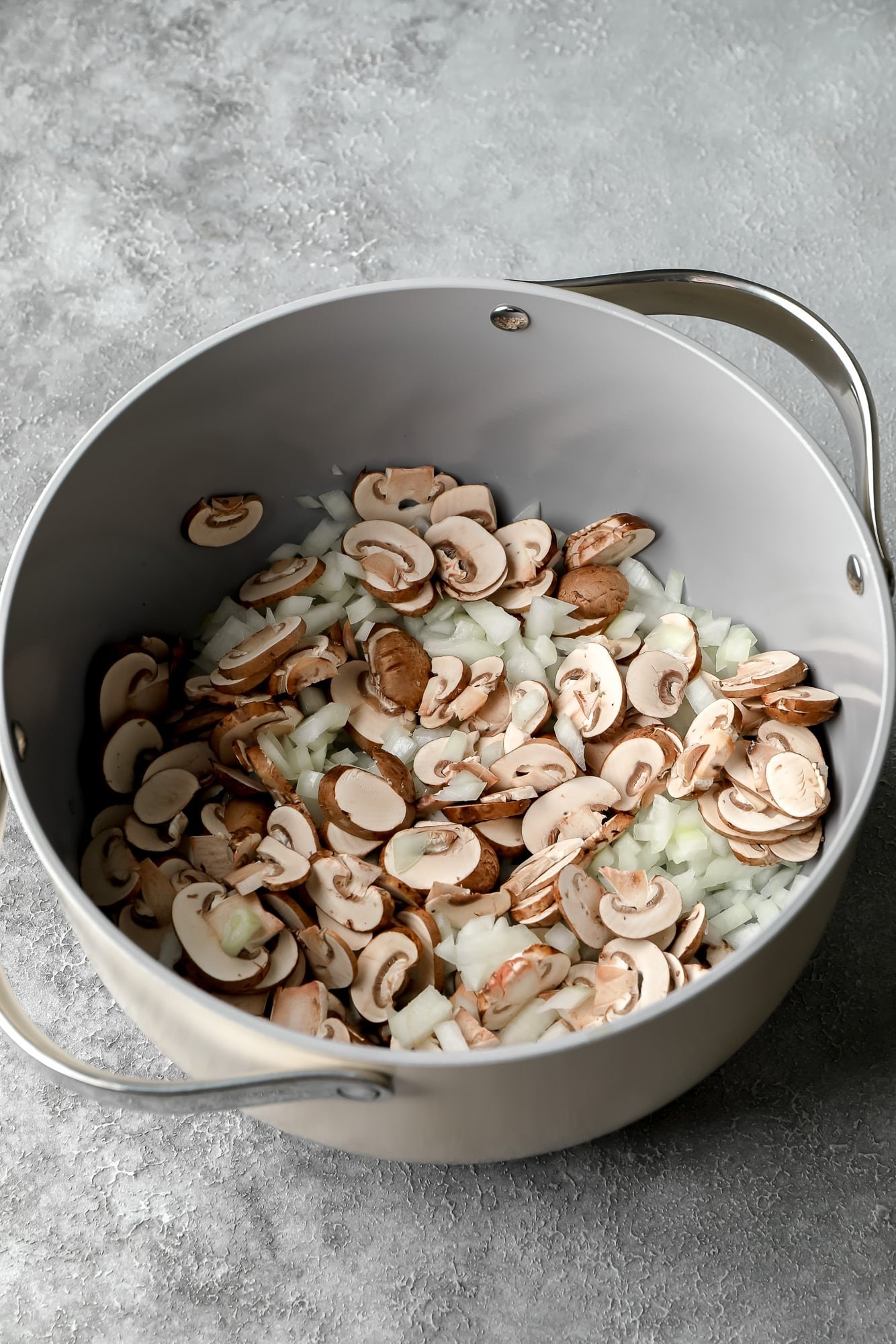 cooking sliced onions and mushrooms in a large grey pot.