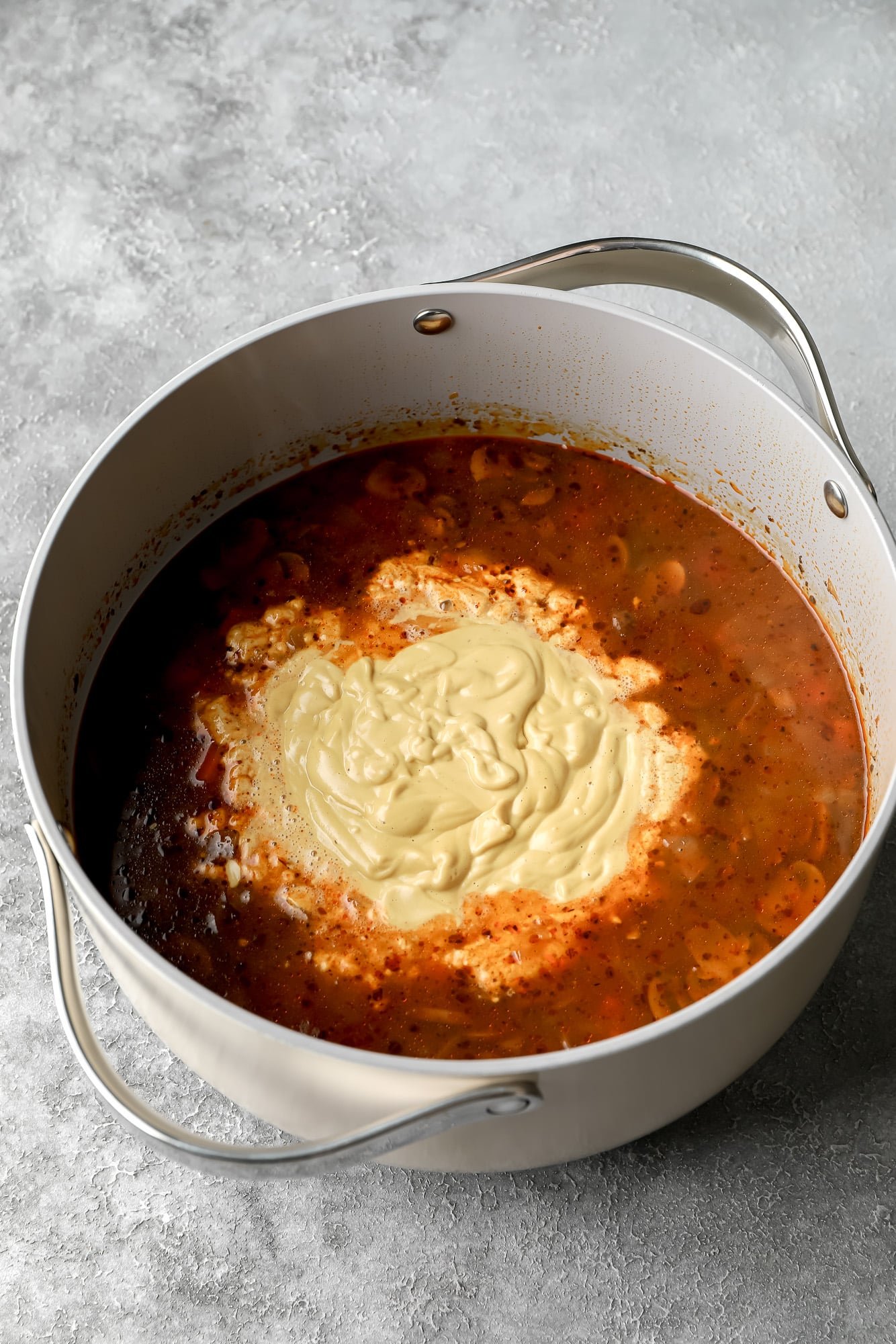 cream sauce poured into a grey pot filled with mushroom soup.