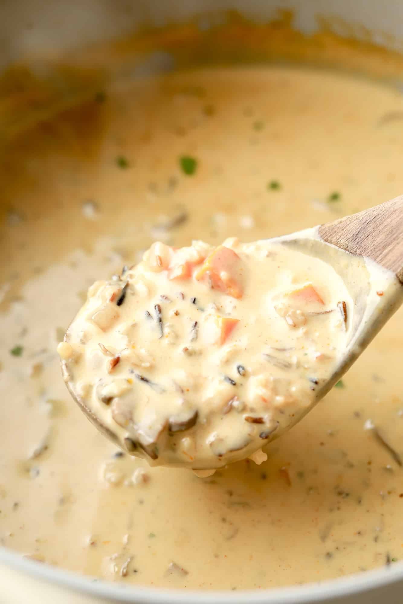 using a wooden spoon to lift a scoop of vegan mushroom soup from a large batch.