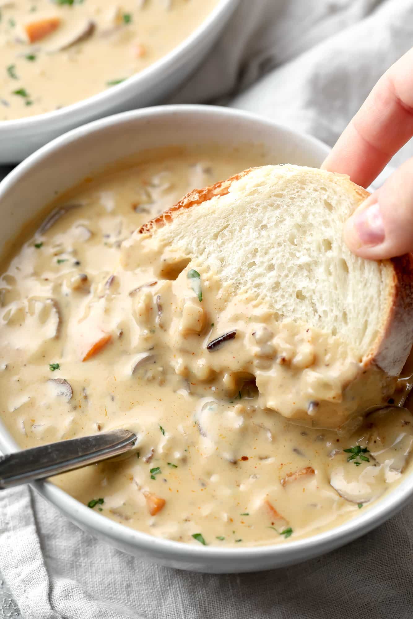 womans hand dipping a piece of bread into a bowl of vegan mushroom soup.