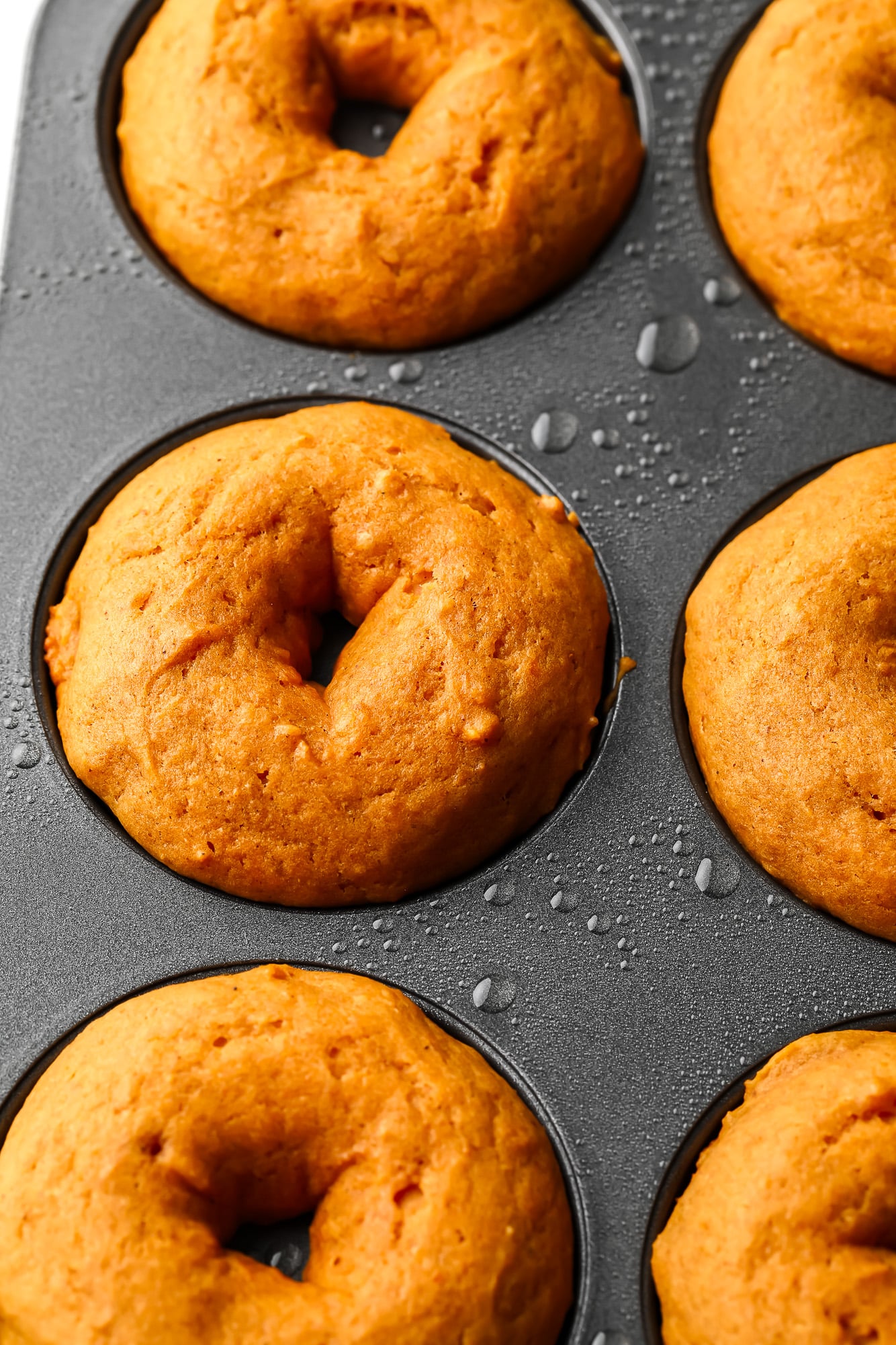 close up on vegan pumpkin donuts in a metal donut pan.