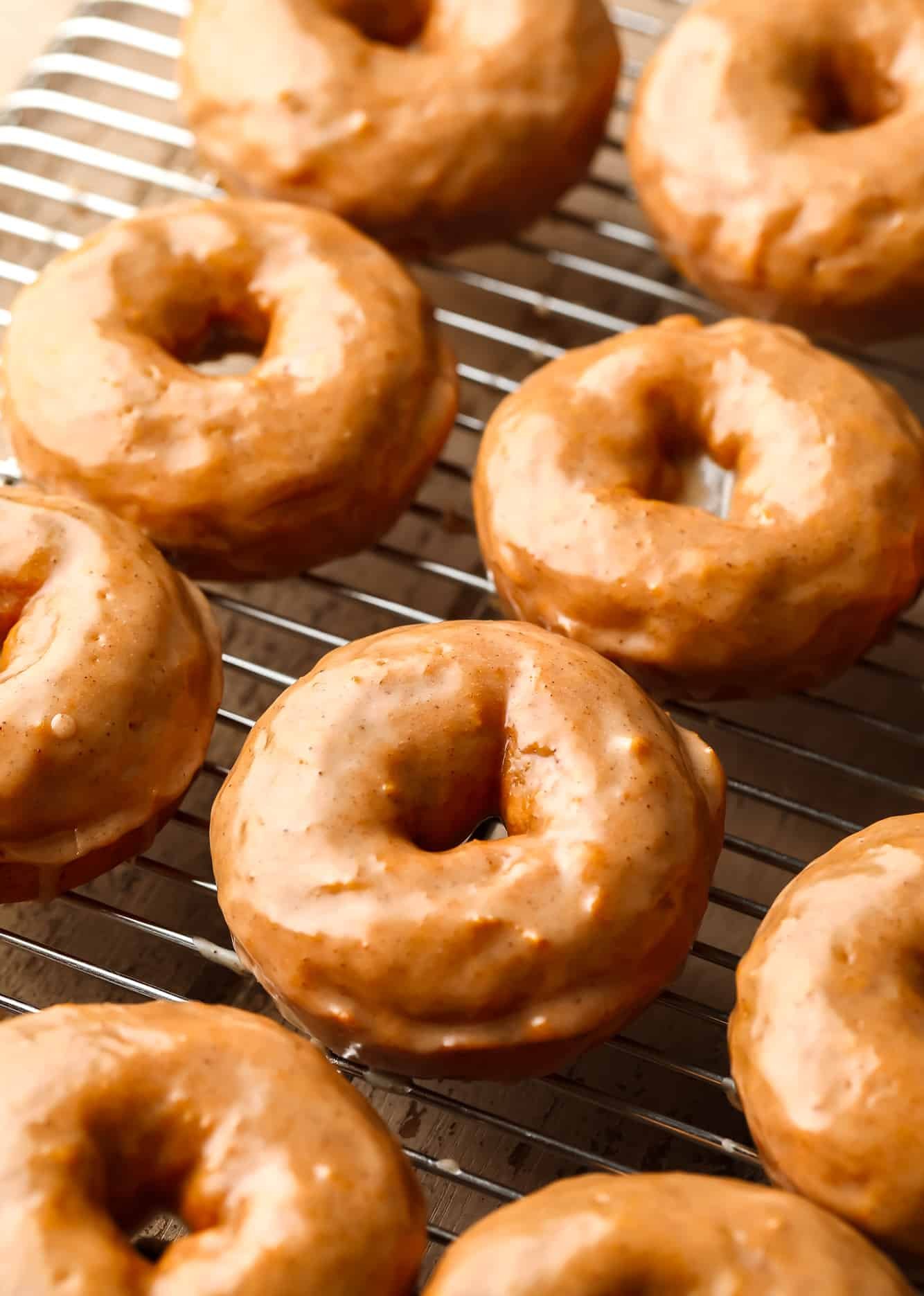 vegan pumpkin donuts coated in a cinnamon maple glaze on a wire cooling rack.