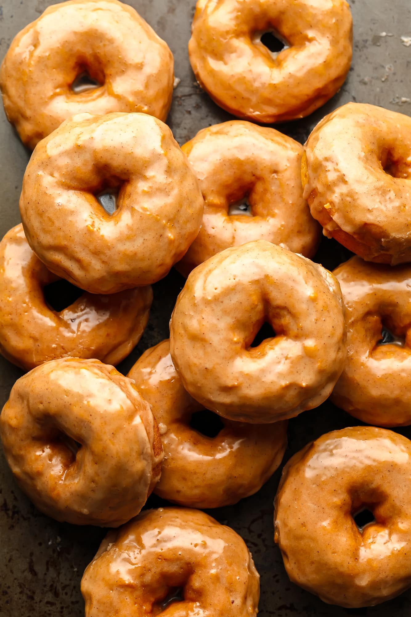 a pile of vegan pumpkin donuts coated with a cinnamon maple glaze.