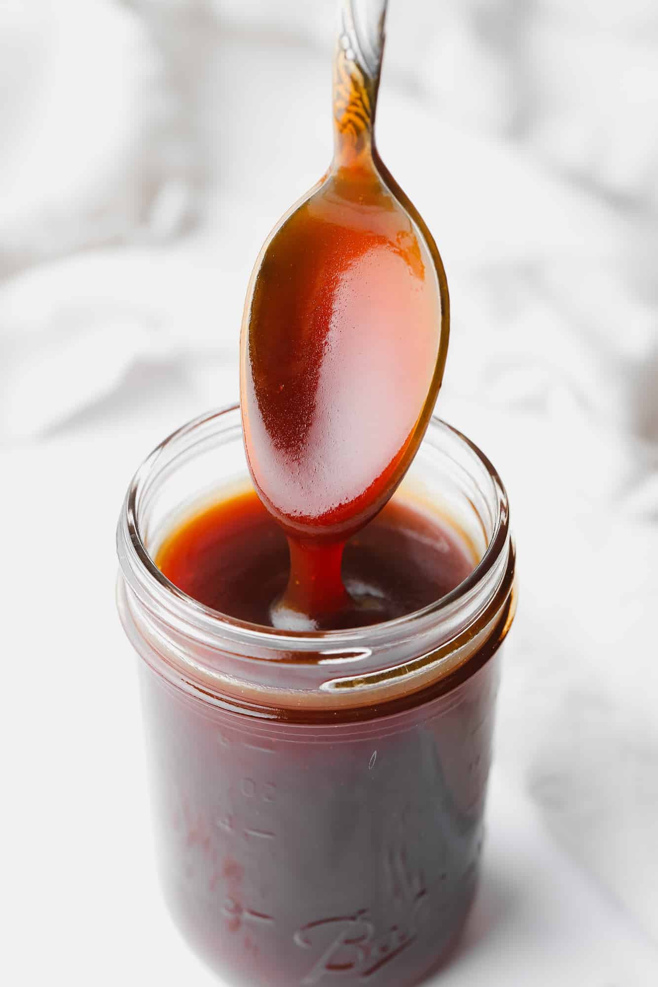 a spoon lifting out of a small jar of vegan salted caramel.