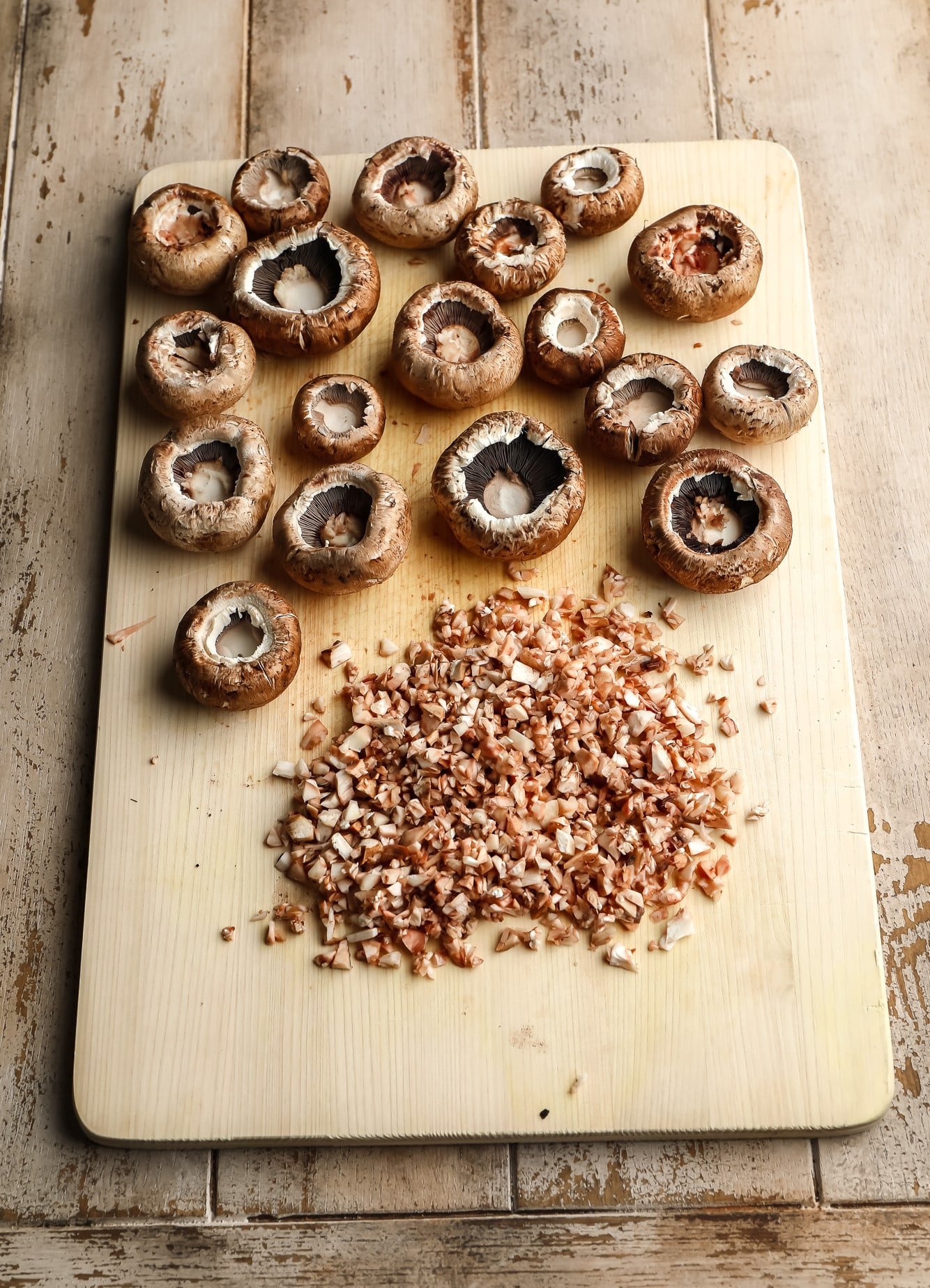 hollow mushroom caps and diced mushroom stems on a cutting board.