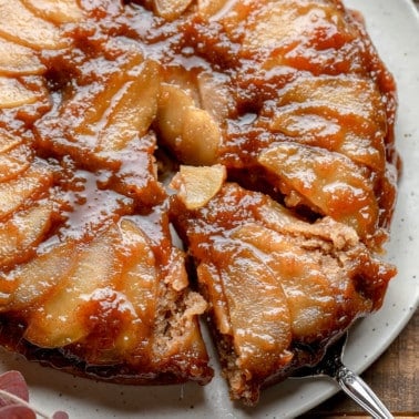 close up on a slice being lifted from an Apple Upside Down Cake on a white plate.