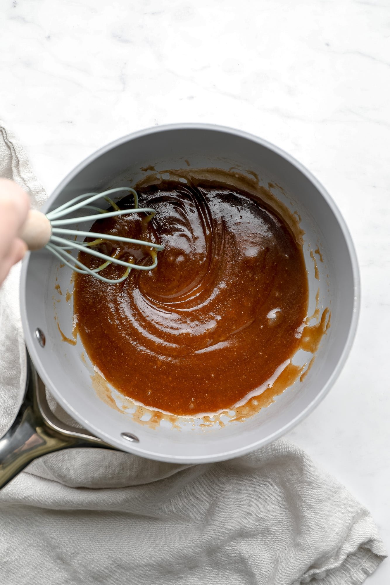 whisking vegan caramel sauce in a grey saucepan.