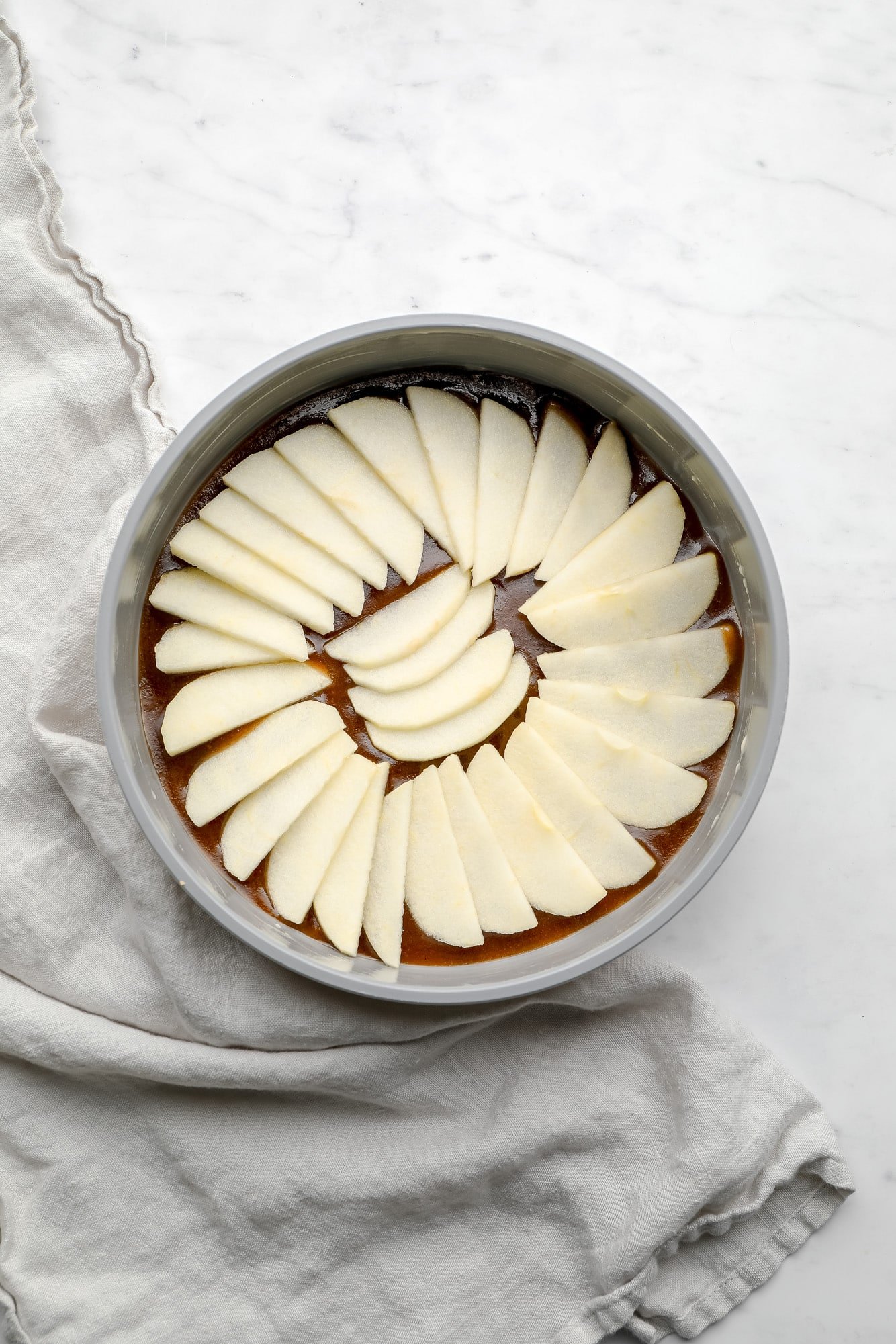 sliced apples layered on top of caramel in a grey round cake pan.