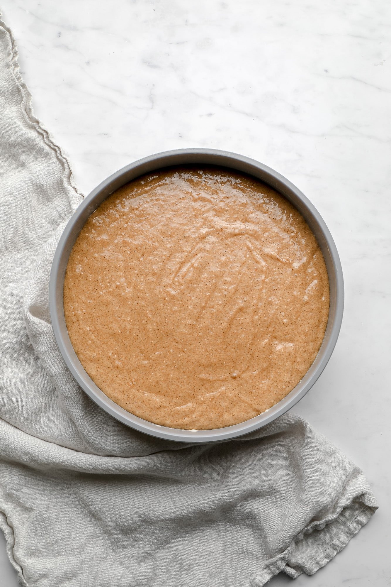 brown cake batter in a round grey cake pan.