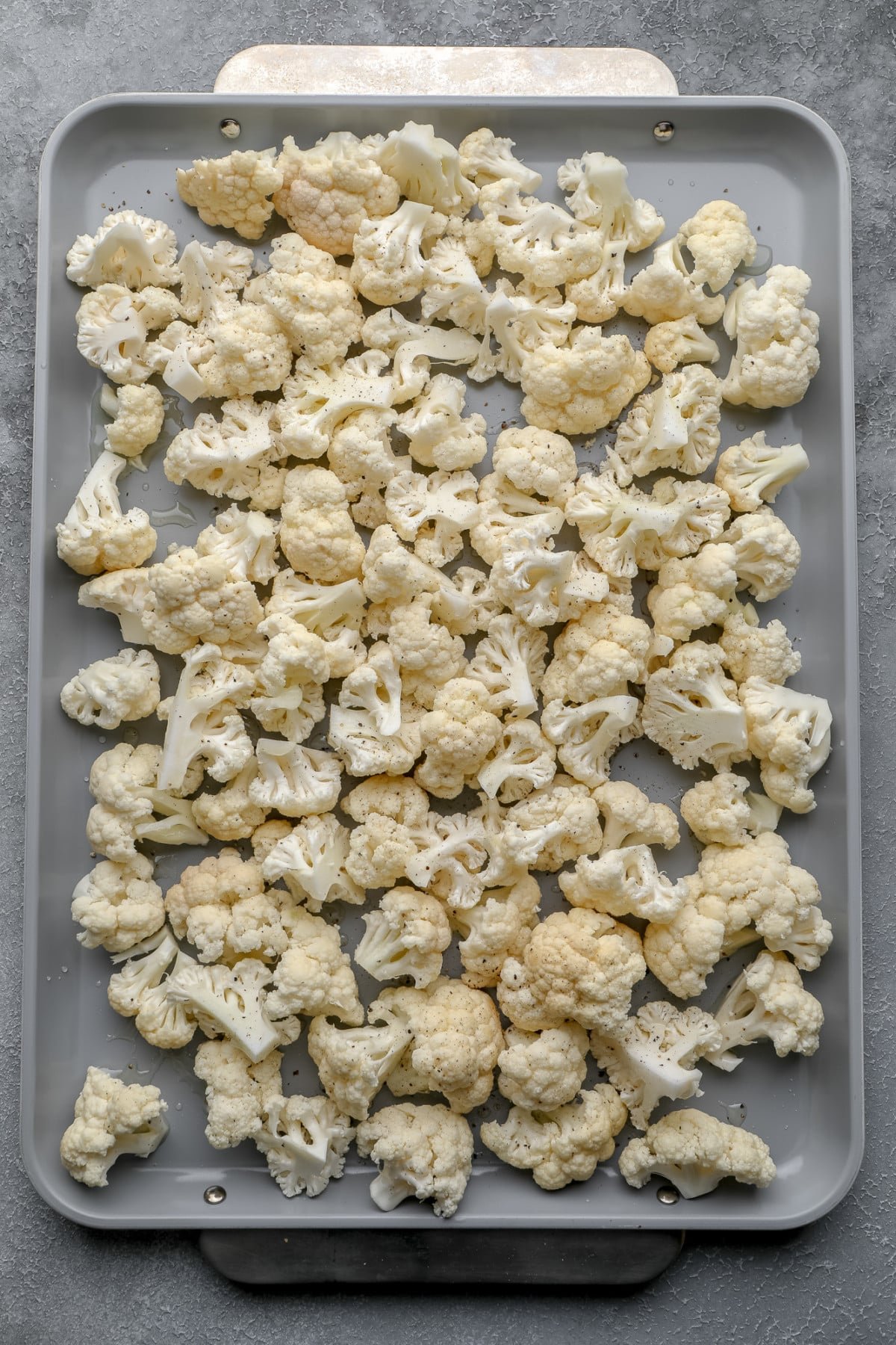raw cauliflower florets on a metal baking sheet.