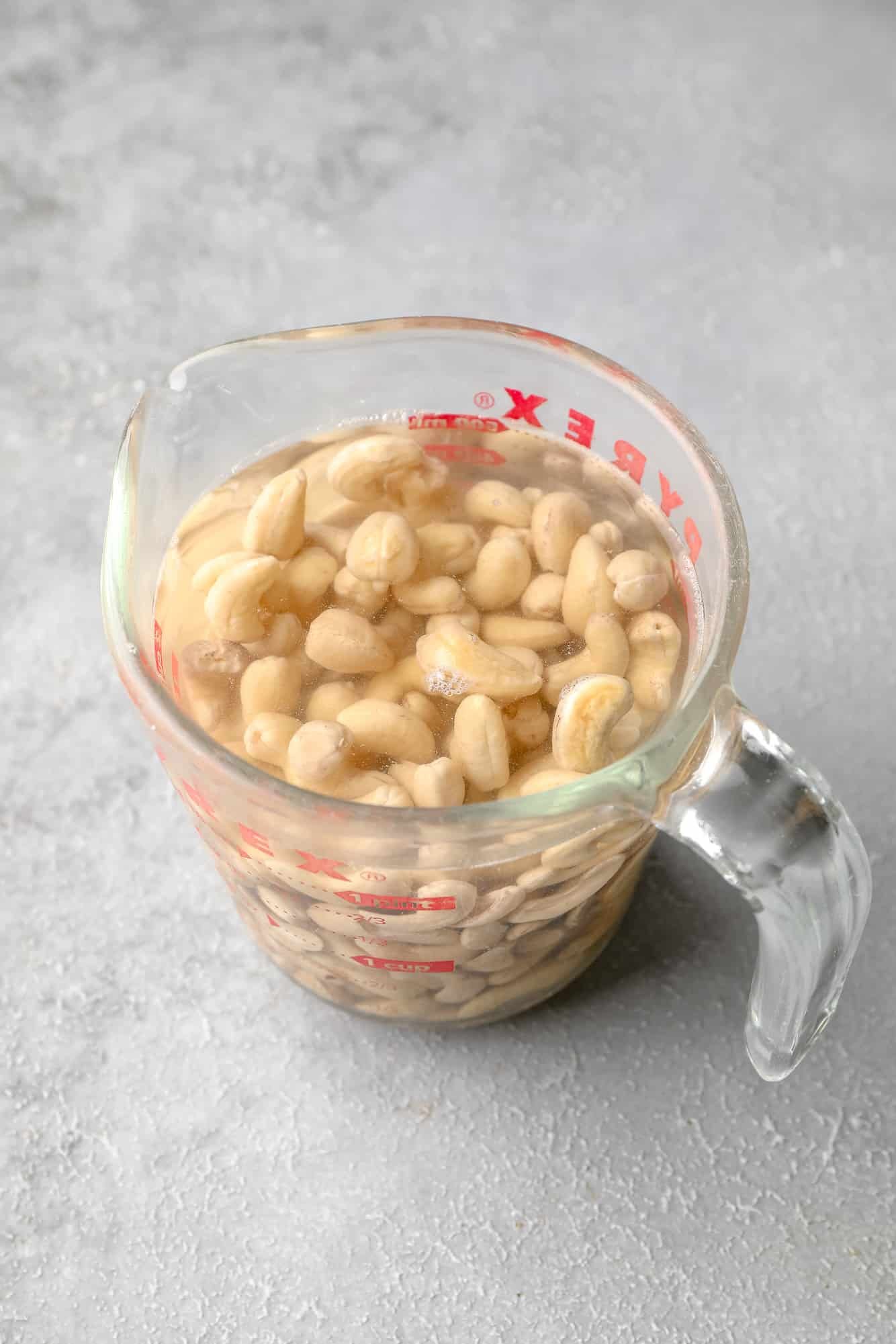 a glass measuring cup full of water and cashews.