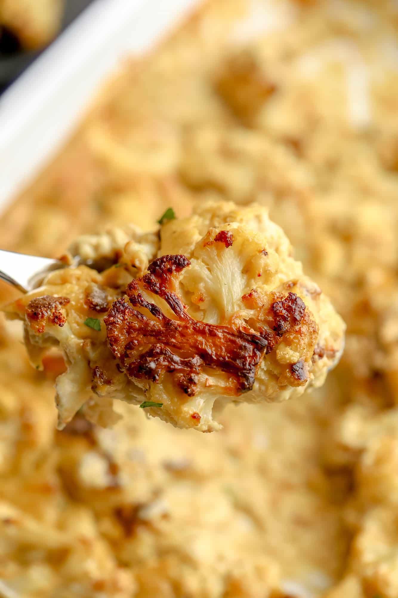 close up on a roasted cauliflower floret smothered in vegan cheese sauce.