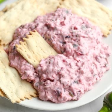 pink cranberry jalapeno dip on a white plate with crackers.