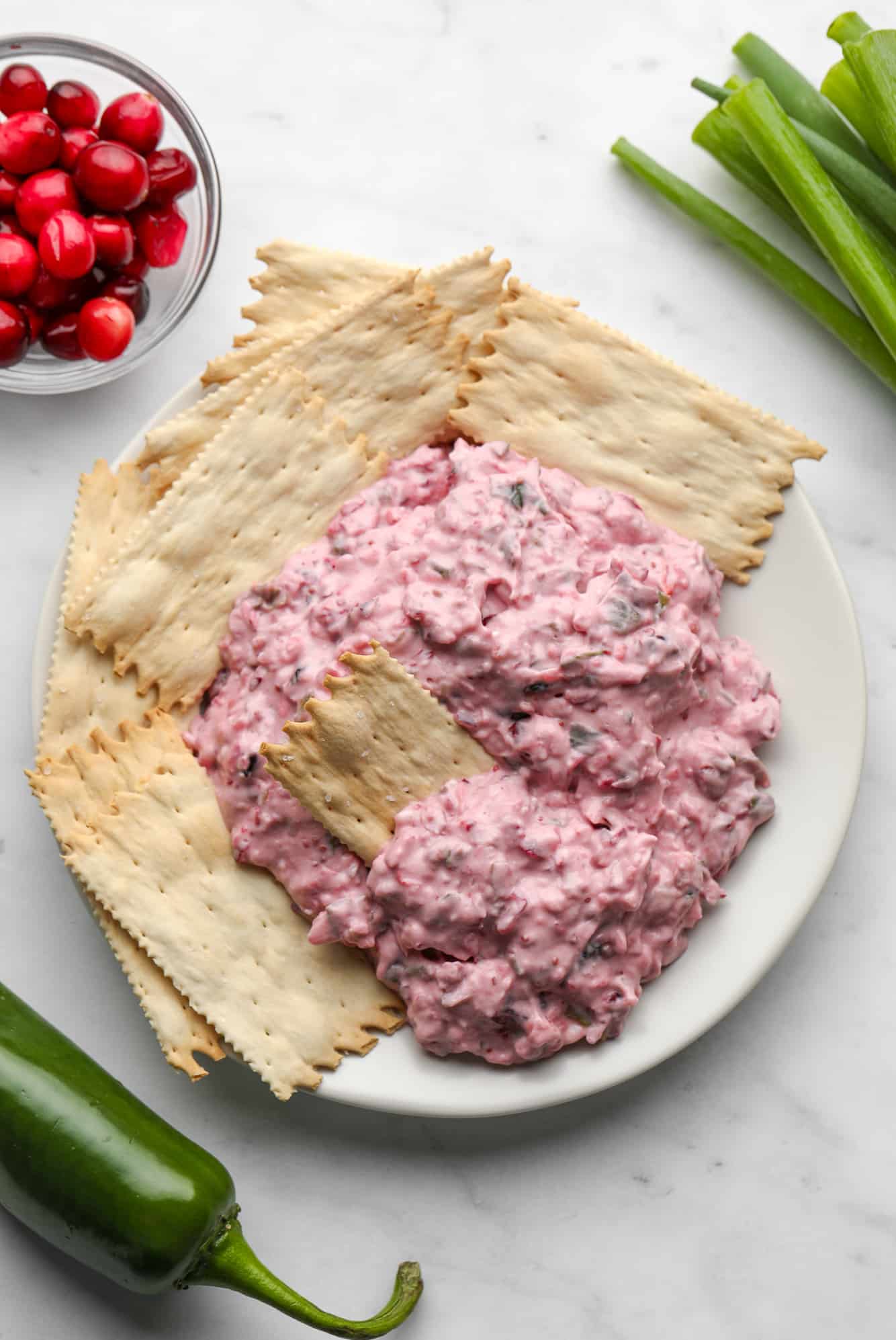 pink cranberry jalapeno dip on a white plate with crackers.