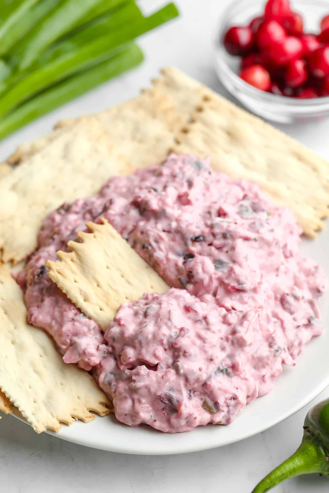 pink cranberry jalapeno dip on a white plate with crackers.