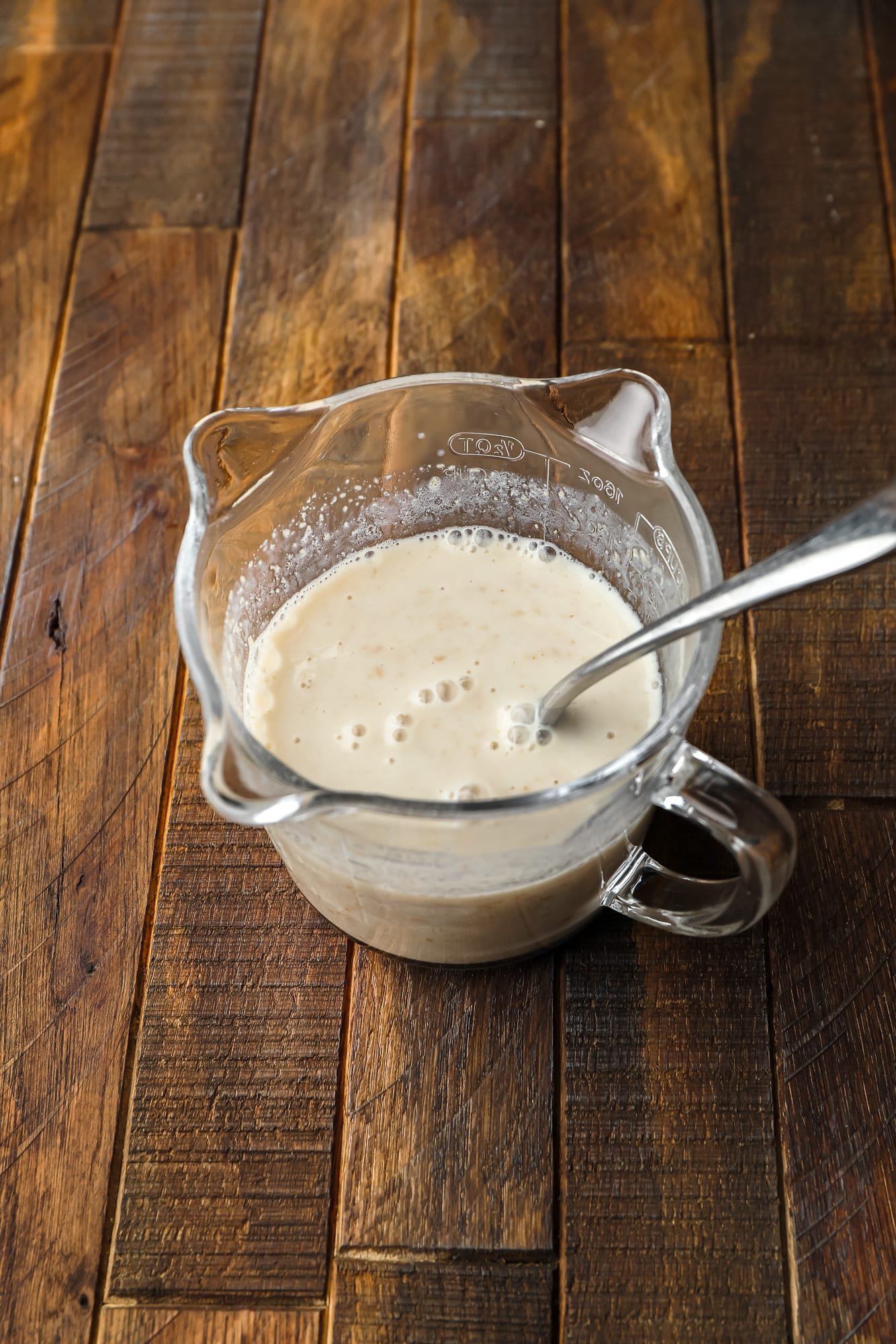 using a metal spoon to stir a milk and flaxseed mixture in a glass measuring cup.