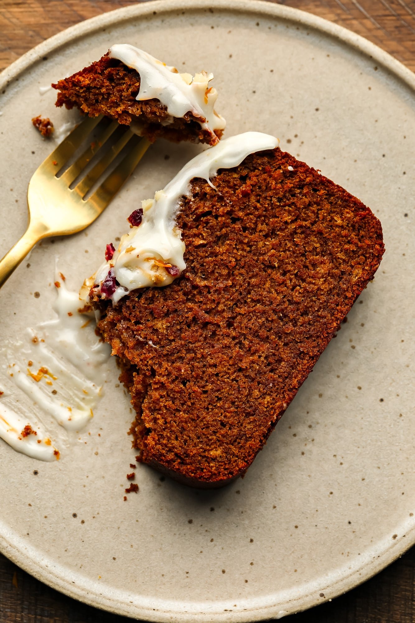 using a fork to eat a slice of a gingerbread loaf on a beige plate.