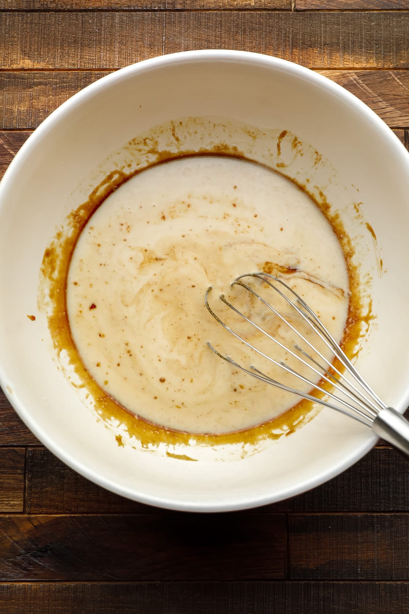 whisking the wet ingredients for a gingerbread loaf in a large white bowl.