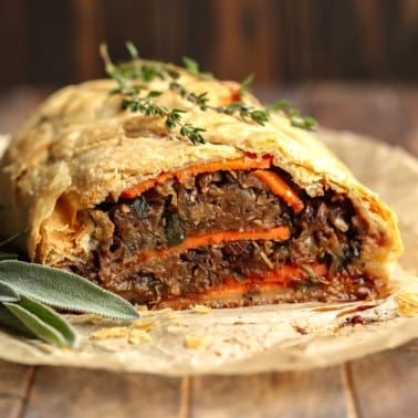 close up on a baked and sliced mushroom wellington topped with fresh thyme.