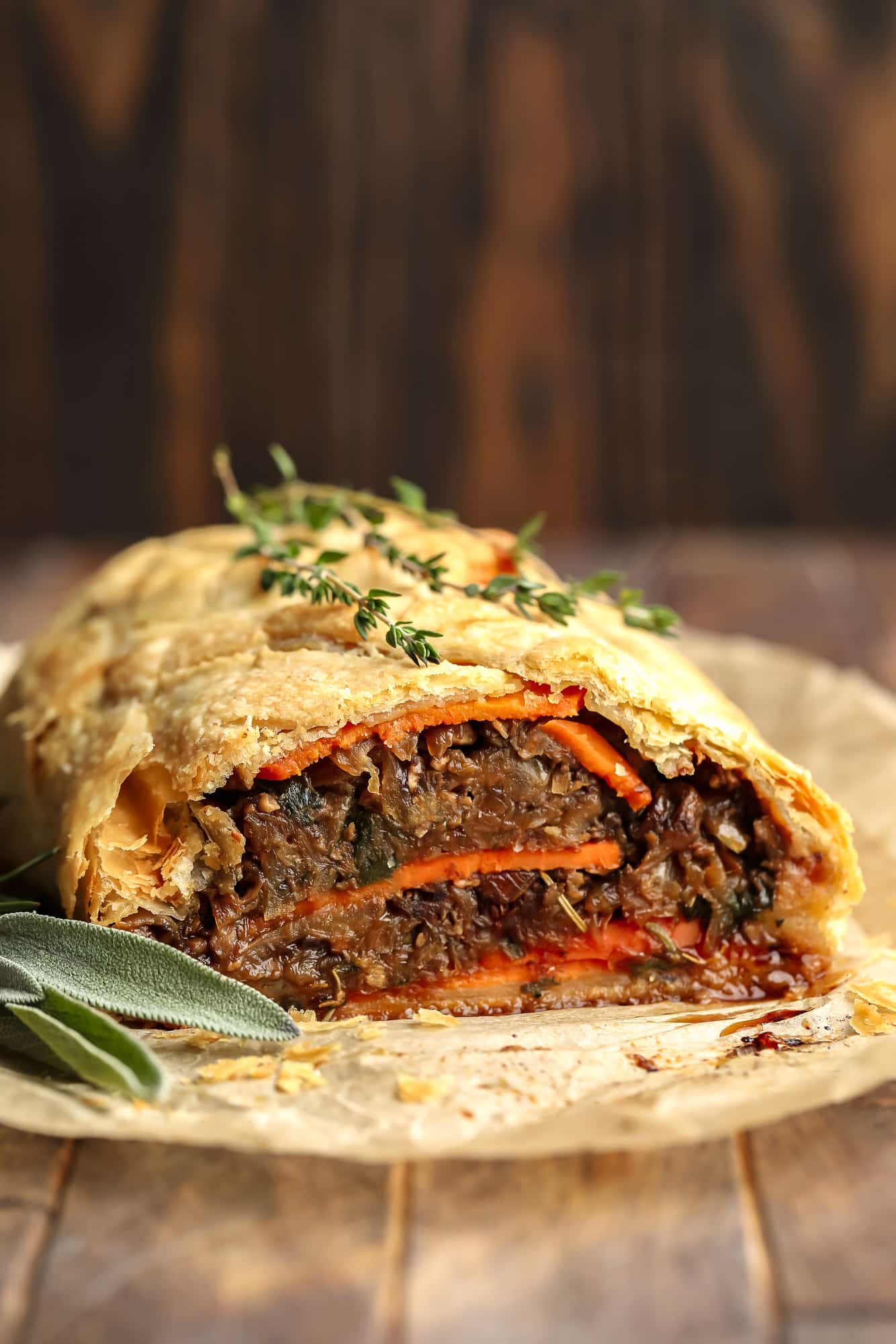 close up on a baked and sliced mushroom wellington topped with fresh thyme.