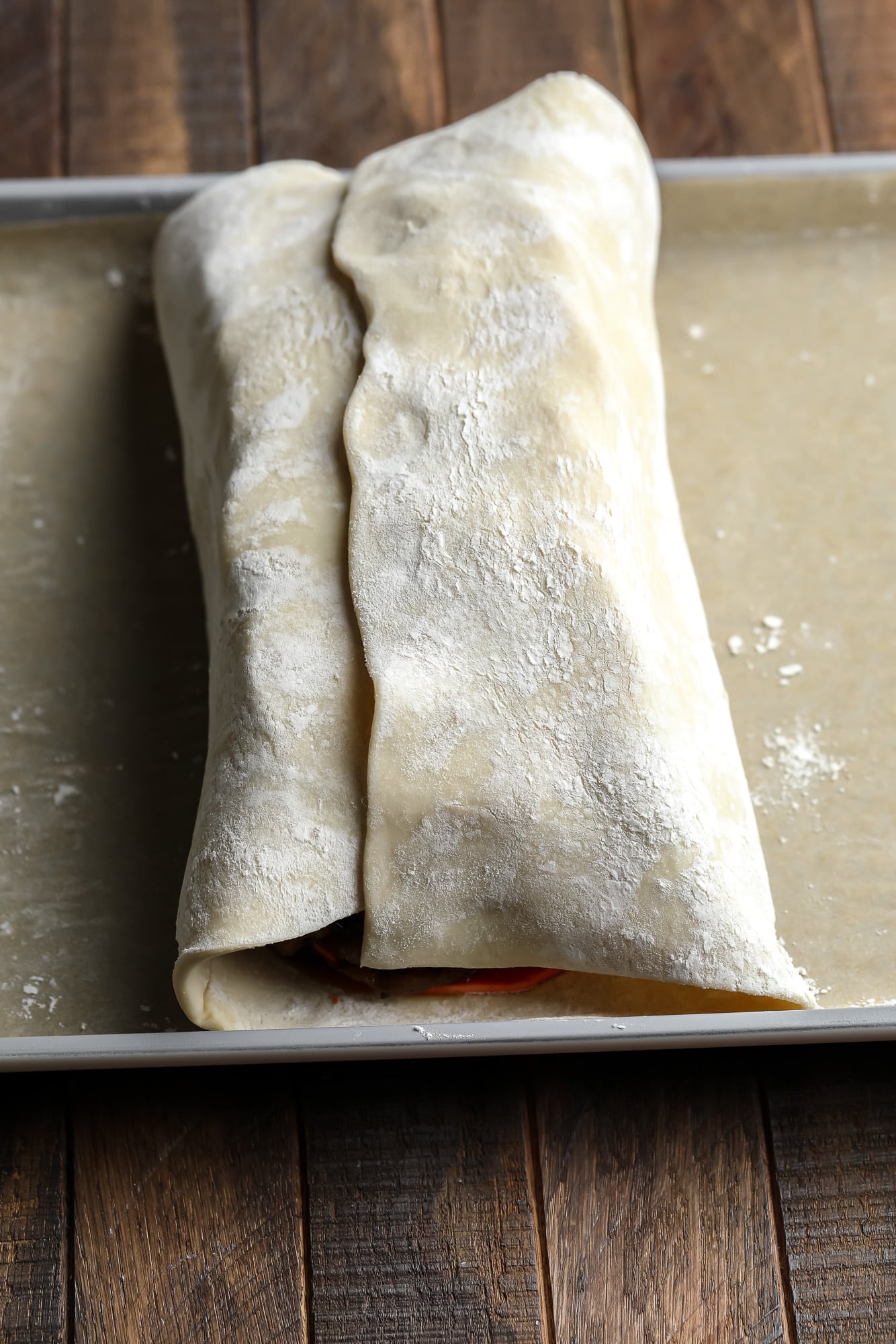 a sheet of puff pastry wrapped around a mushroom filling for mushroom wellington on a baking sheet.