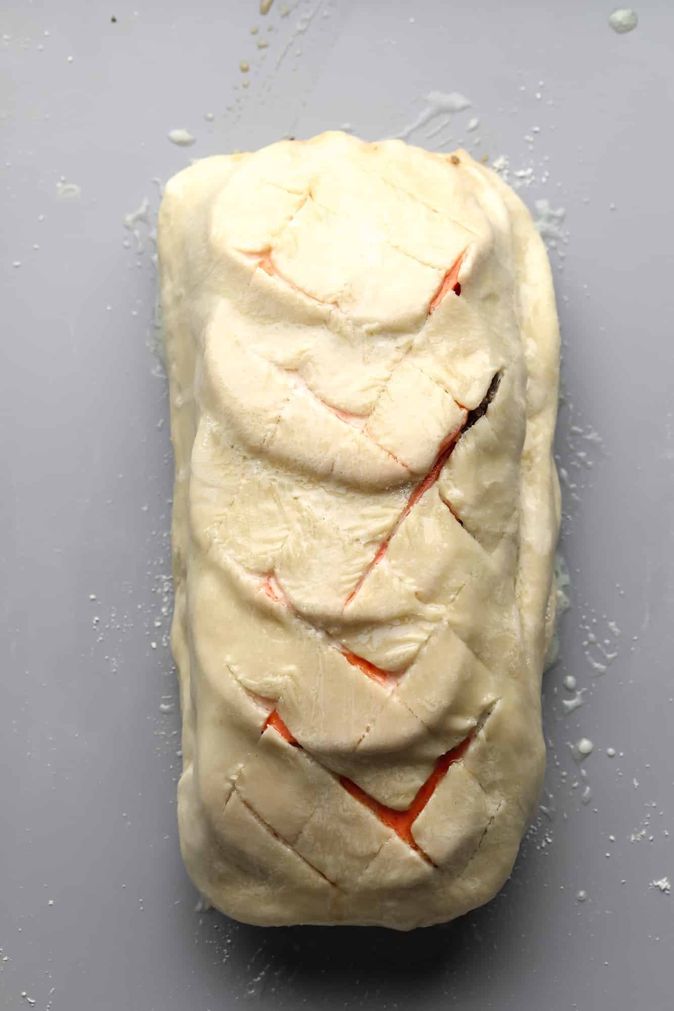 a scored unbaked mushroom wellington on a grey sheet pan.