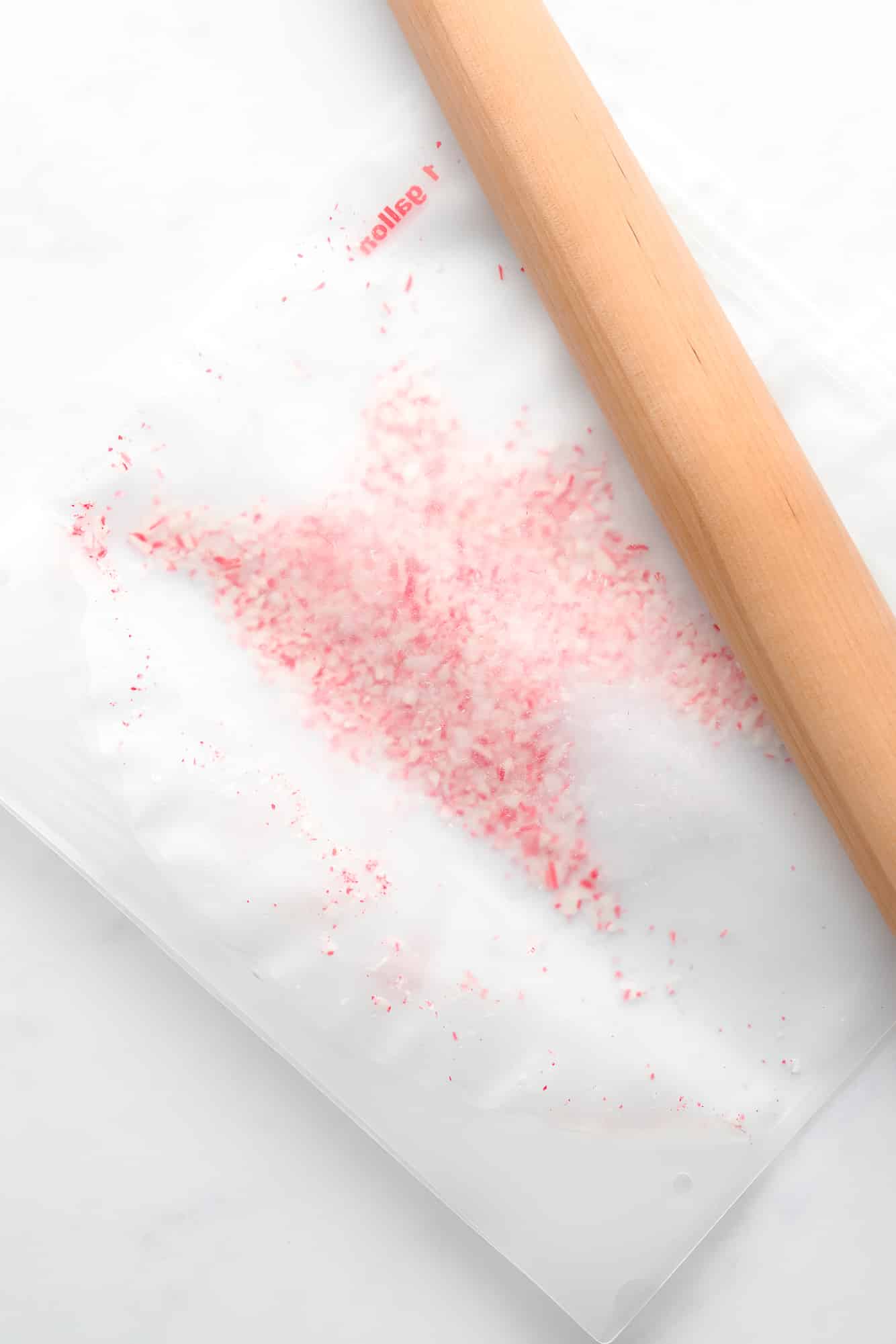 using a wooden rolling pin to crush candy canes in a clear plastic bag.