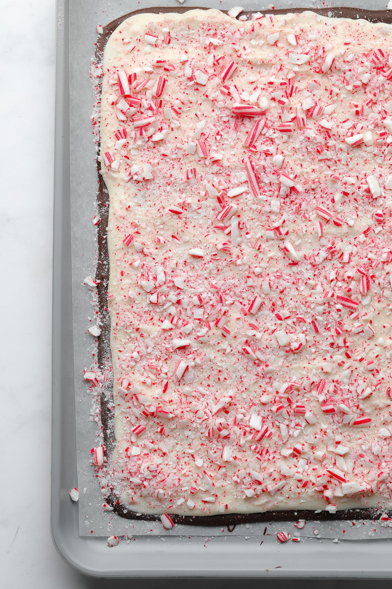 vegan peppermint bark topped with crushed candy canes on a parchment-lined baking sheet.