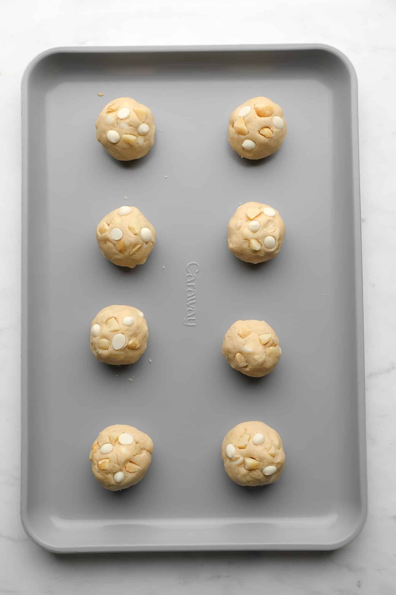 Vegan White Chocolate Macadamia Nut Cookie dough balls on a metal baking sheet.