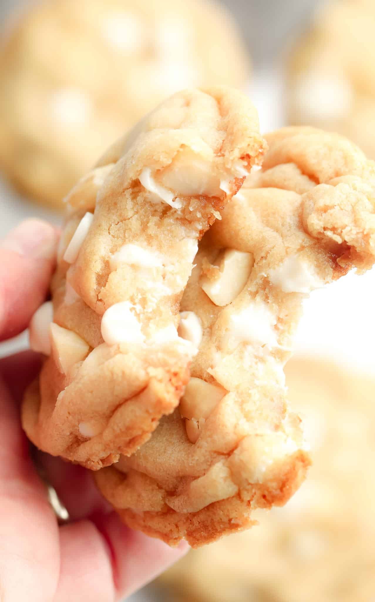 womans hand holding up two Vegan White Chocolate Macadamia Nut Cookies with bites taken out of them.