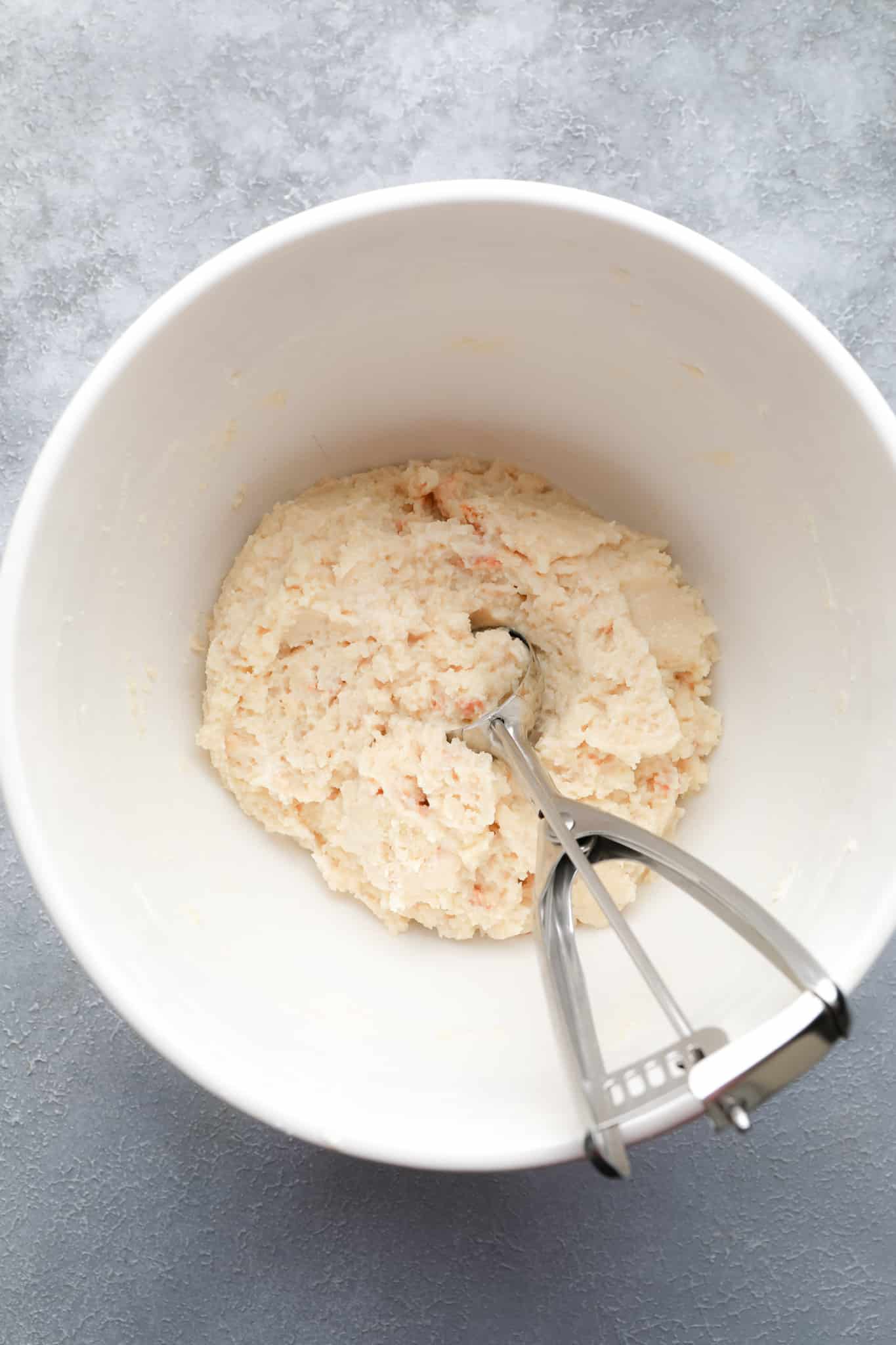 using a cookie scoop to lift a scoop of a crumbled cake and frosting mixture from a white bowl.
