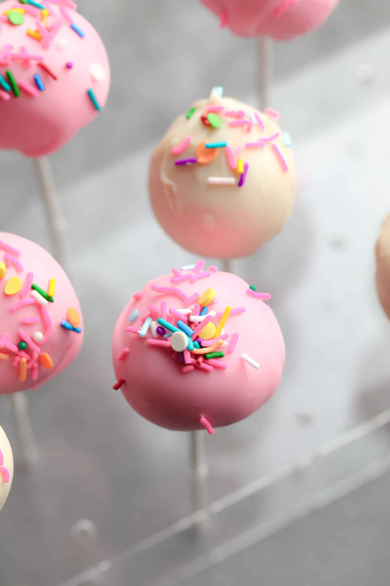 pink and white vegan cake pops decorated with colorful sprinkles.