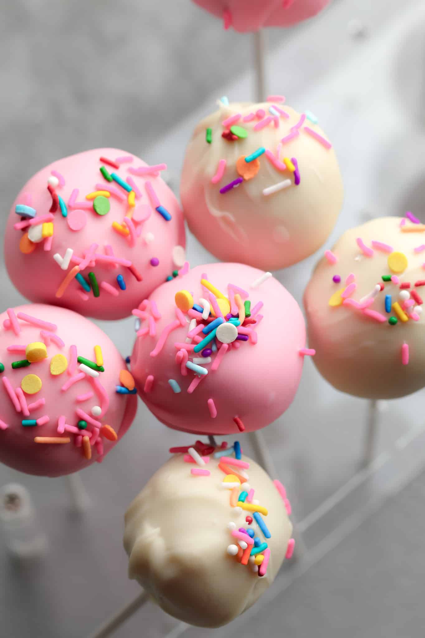 pink and white vegan cake pops decorated with colorful sprinkles.