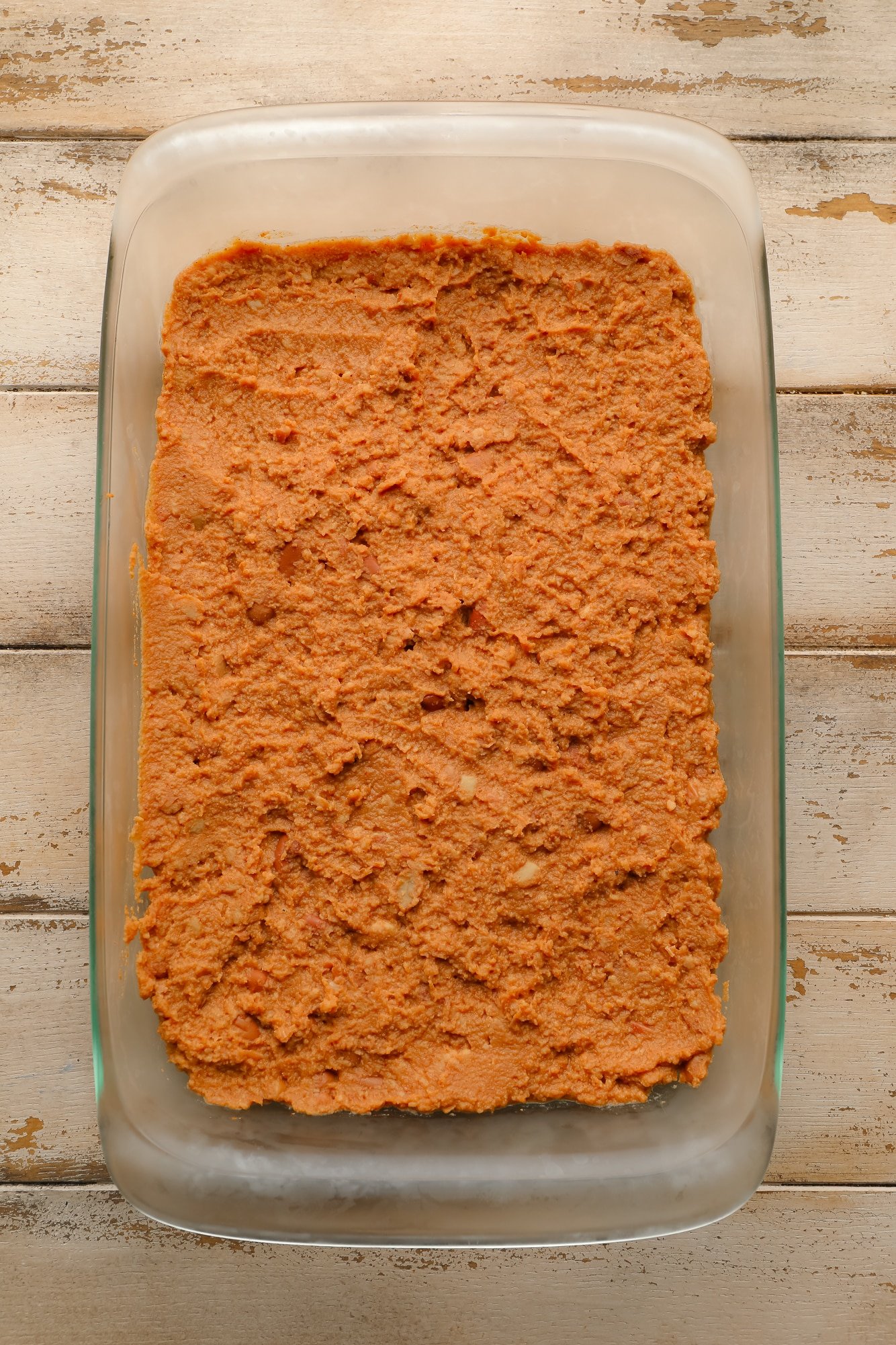 refried beans spread on the bottom of a glass casserole dish.