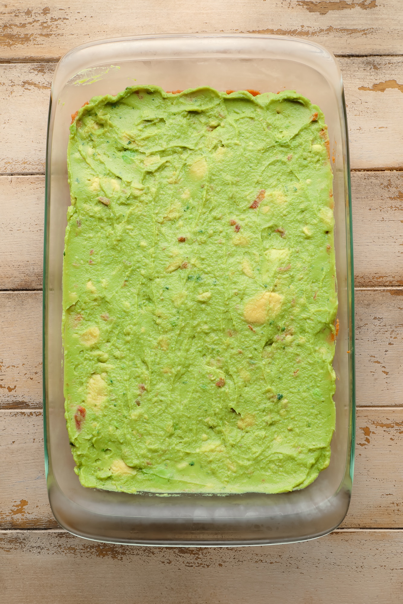 guacamole spread on top of refried beans in a glass casserole dish.