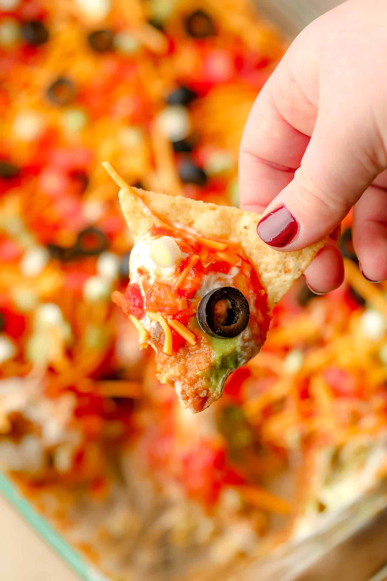 womans hand holding a tortilla chip that's been dunked in vegan 7 layer dip.