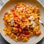 Vegan Buffalo Mac and Cheese topped with white vegan ranch and hot sauce in a beige bowl.