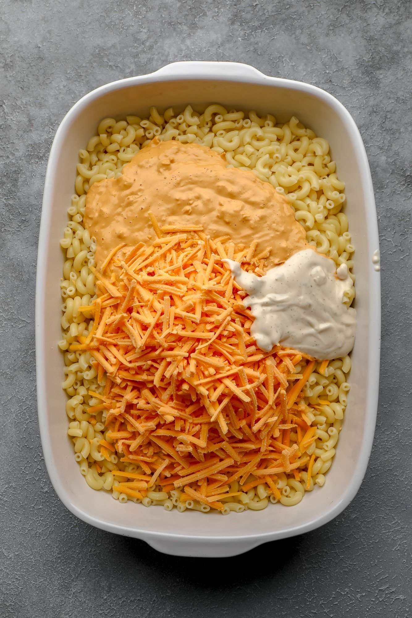 assembling the ingredients for Vegan Buffalo Mac and Cheese in a large white casserole dish.