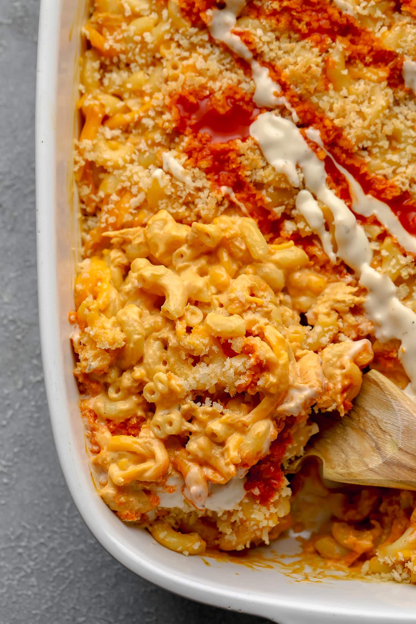 using a wooden spoon to remove a scoop of Vegan Buffalo Mac and Cheese from a large white casserole dish.