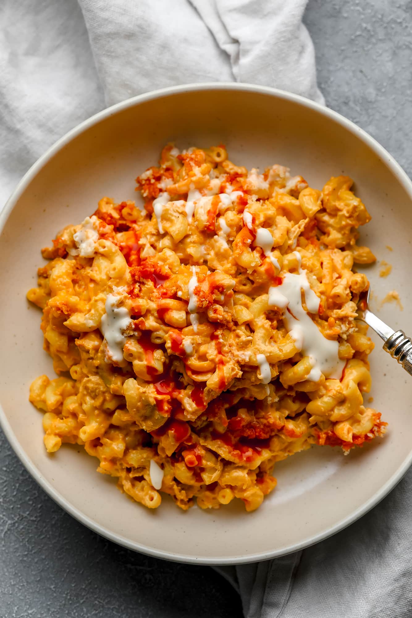 Vegan Buffalo Mac and Cheese topped with white vegan ranch and hot sauce in a beige bowl.