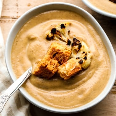 roasted cauliflower soup topped with croutons and charred cauliflower florets in a white bowl.