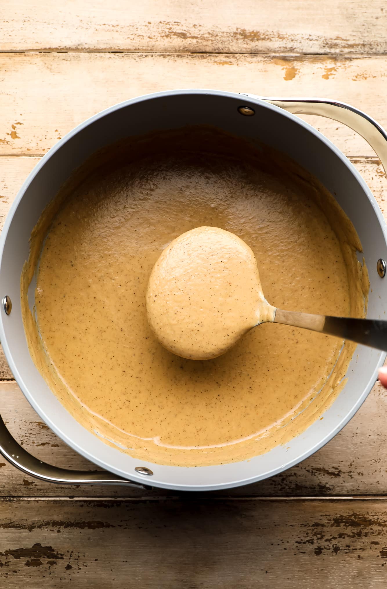 a ladle lifting a scoop of cauliflower soup from a large batch in a grey pot.