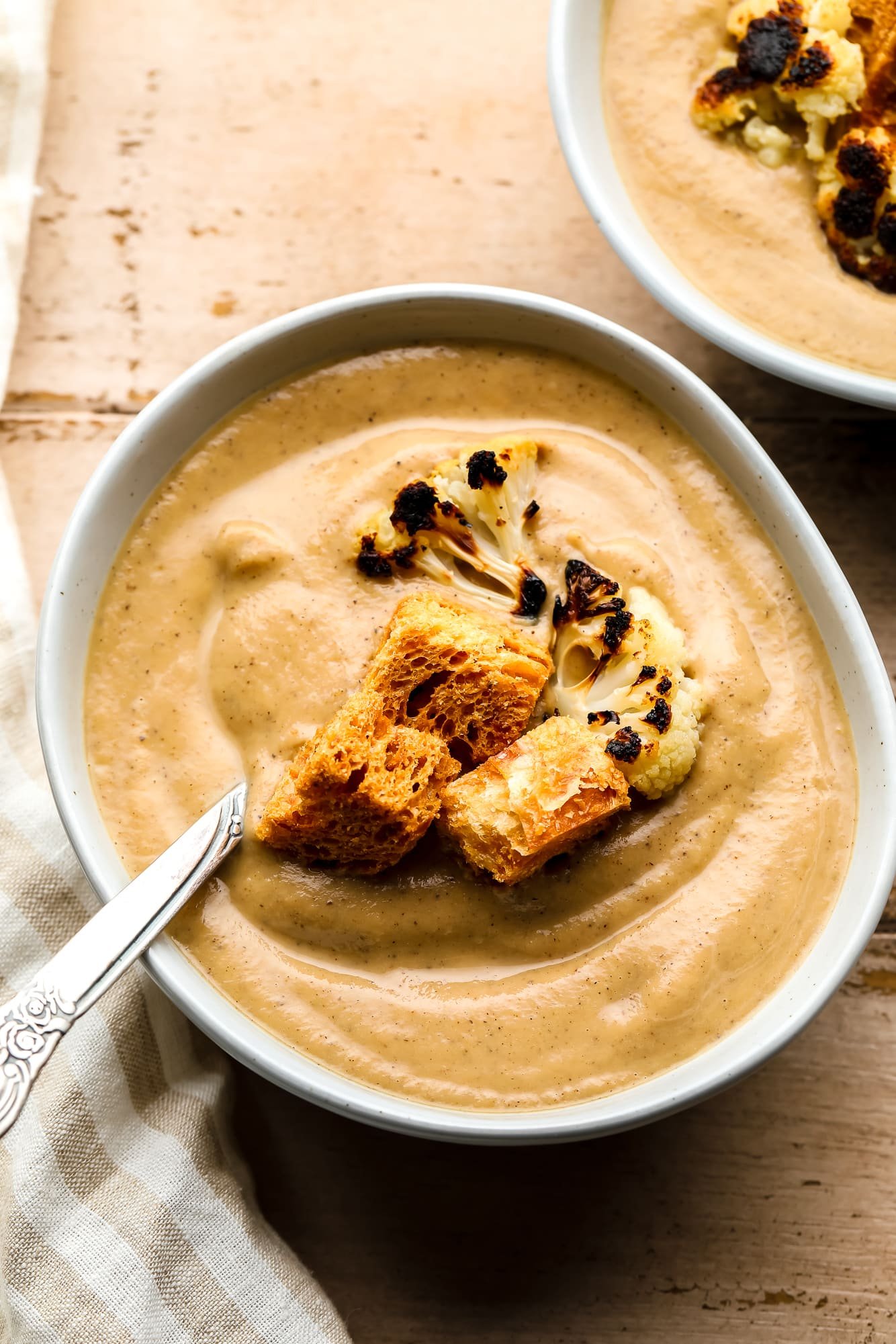 roasted cauliflower soup topped with croutons and charred cauliflower florets in a white bowl.