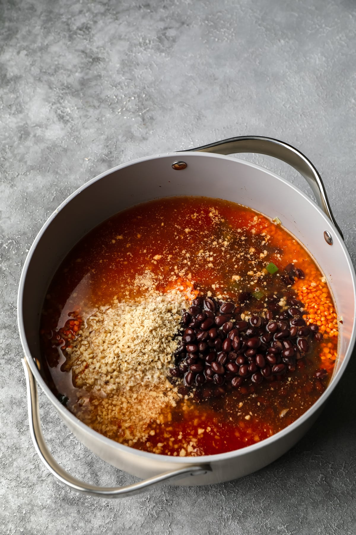 grey pot with broth, beans, chopped walnuts and lentils