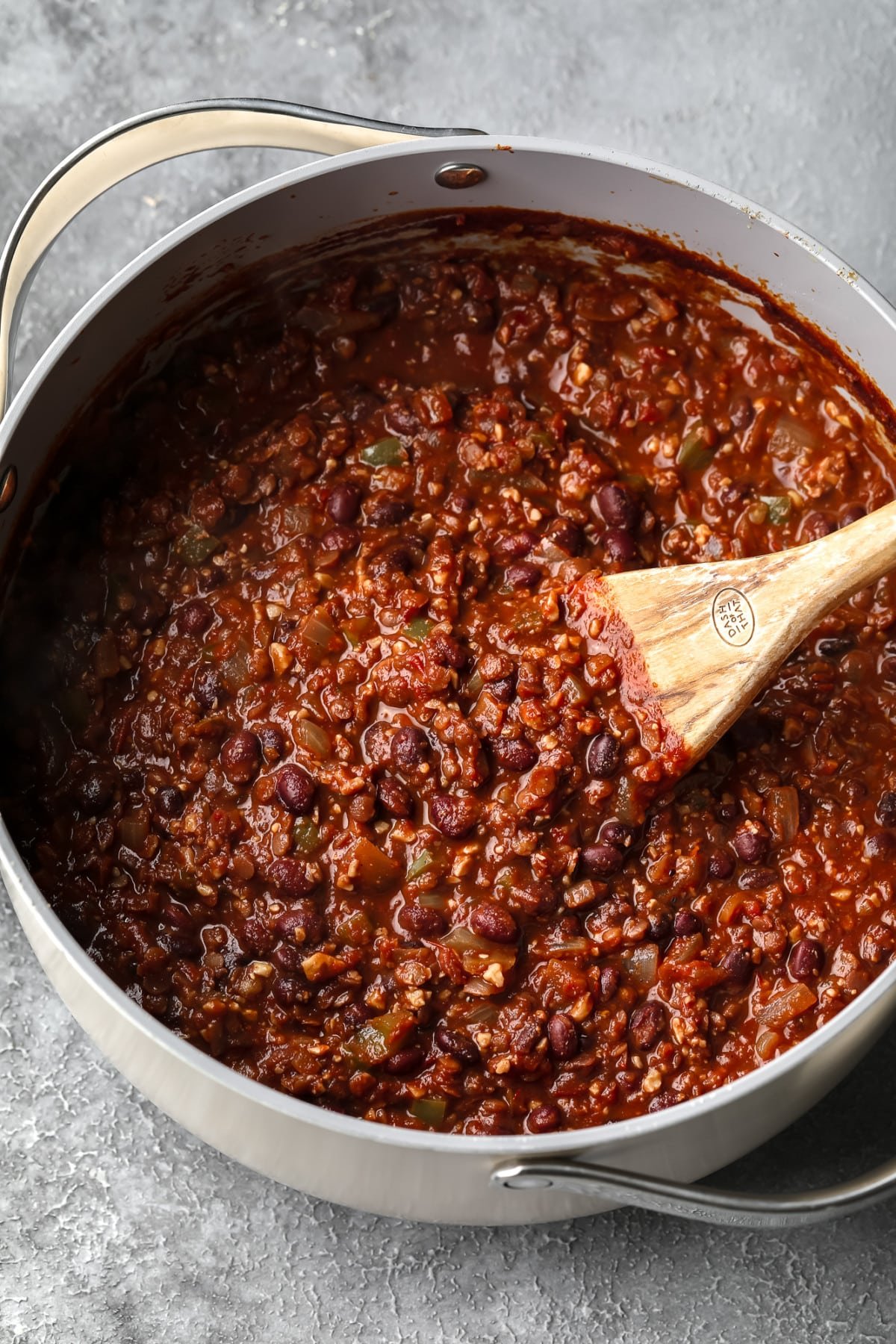 grey pot on grey background full of lentil chili with a wood spoon stirring it