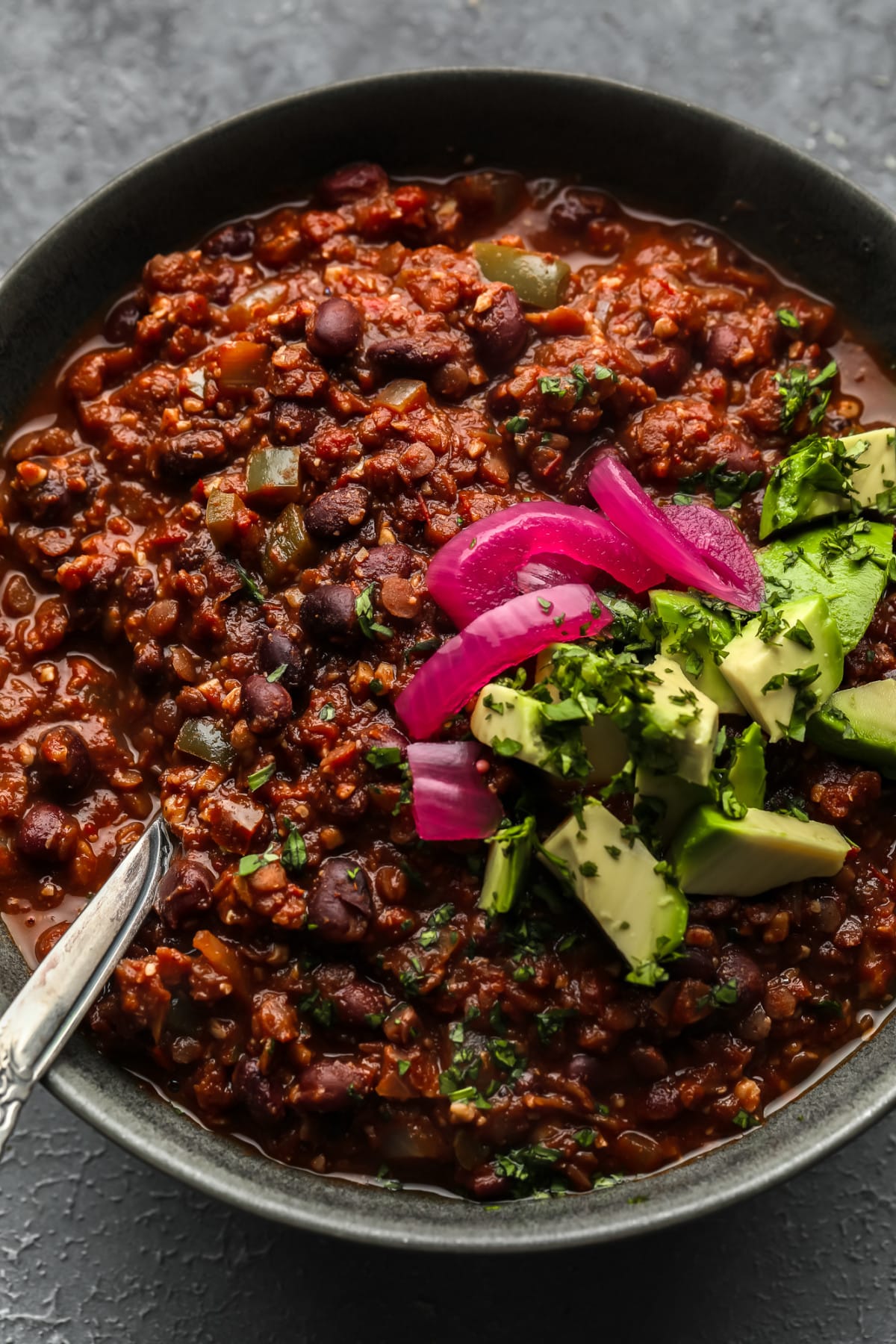 dark grey bowl of lentil chili with pickled onions, avocado and cilantro